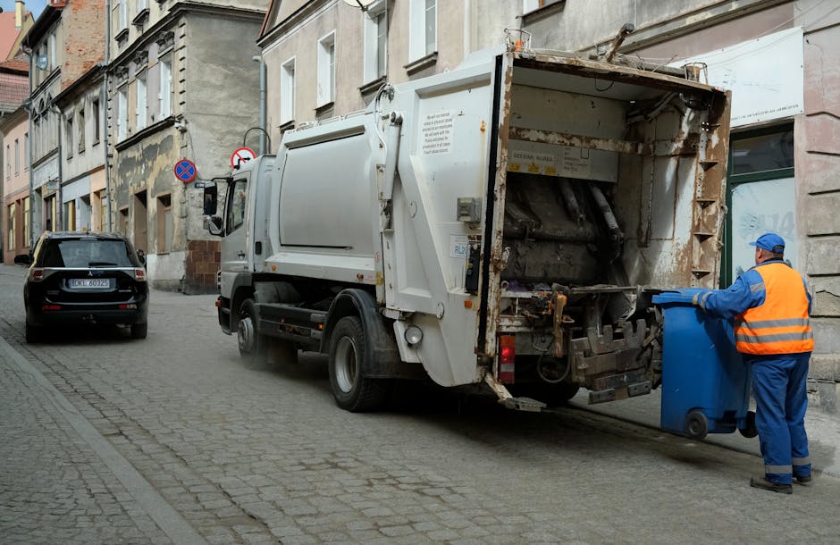 A person wearing a white shirt is seen disposing of a crumpled brown paper bag into a grey rubbish bin with a partially open lid, which is positioned on a wooden surface. The bag being thrown away app
